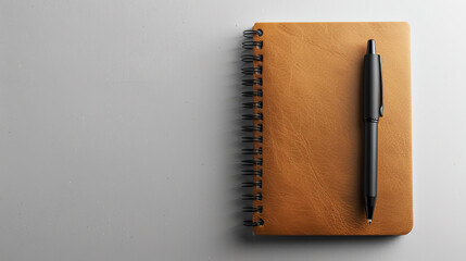 Top view of a leather notepad with a black pen lying next to a light gray background