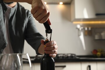 Man opening wine bottle with corkscrew indoors, closeup. Space for text