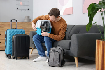 Travel with pet. Man holding carrier with cute cat on sofa at home