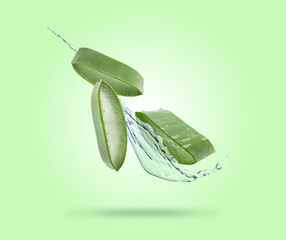 Sliced aloe vera leaf and splash of juice on green background