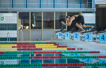 Professional female swimmer in a black open back kneeskin suit, standing on the starting block and...