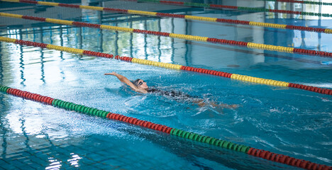 Female athlete in action, performing the backstroke swim technique in the indoor lap pool....