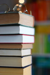 High stack of books on the table. Colorful rainbow bookshelf in the background. Selective focus.