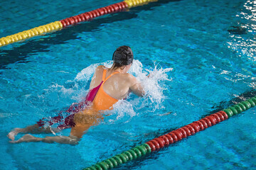 Female swimmer using breaststroke technique to swim an indoor lap pool. Competitive swimming concept.