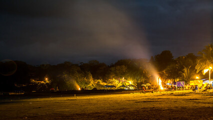 Nocturnal human activity on the beach distant bonfires smoldering under artificial light