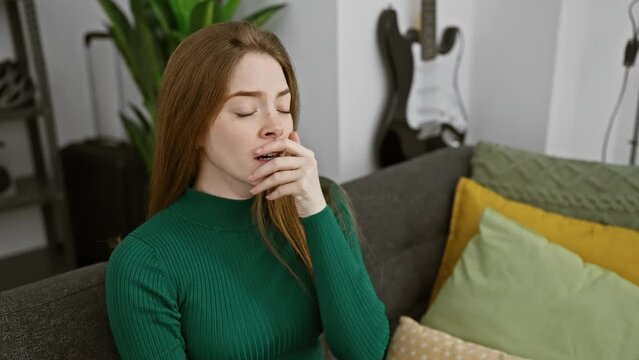 Sleep-deprived young blonde woman in sweater trying to pry open her eyes with fingers, yawning from morning fatigue at home in her bedroom, a humorous display of tiredness