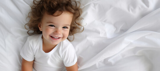 Portrait of a happy small child baby lying in bed on white sheets smiling brightly happily with copyspace