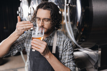 Worker man sommeliers taste drink on Brewery factory. Expert brewer in apron holds glass of craft beer and checking quality and color