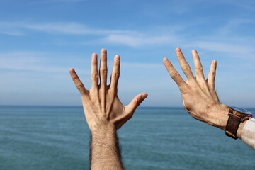 Hand doing,showing number gesture symbol nine on blue summer sky nature background. Gesturing...