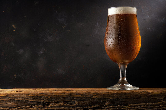 Glass of light beer on a wooden table. Dark background. Drink concept.