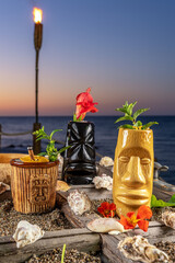 Different tropical Tiki cocktails on the sea background during sunset.
