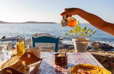 Close up of breakfast served on a typically Greek tavern table at sunrise with hand pouring honey...