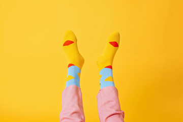Playful feet up in the air with bright yellow socks featuring red lips pattern on a vivid yellow background.