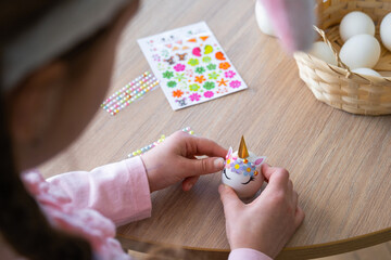 A cute girl with pink bunny ears makes an Easter craft - decorates an egg in the form of a unicorn...