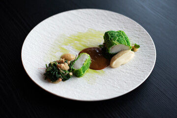 Fish in cabbage with spoon dumpling, spinach and beans on white plate.
