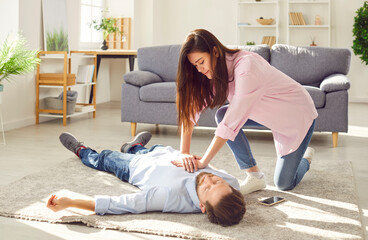 Young woman doing CPR on unconscious man lying on the floor at home. Wife trying to resuscitate her...