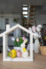 Tiny house of cozy home with Easter decor with rabbit and eggs on table of kitchen. Building,...