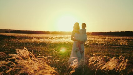 Mother carries girl home after walk in evening field. Mother enjoys motherhood carrying daughter in...