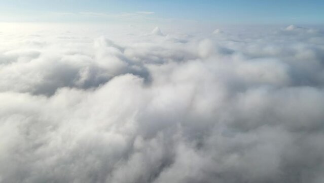 Aerial shot of flying over a layer of soft clouds at dawn