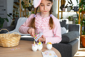 A cute girl with pink bunny ears makes an Easter craft - decorates an egg in the form of a unicorn...