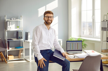 Portrait of young happy attractive bearded business man in white shirt and glasses sitting at the...