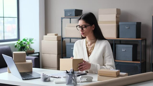Concentrated Caucasian businesswoman working in storage office, preparing package to sending order to customer. Preparation parcel to shipping. Online shop concept.