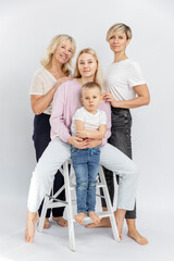 Happy smiling family. Three generations of women and a little boy in white T-shirts and jeans. Full height. Love and tenderness. White background. Vertical.