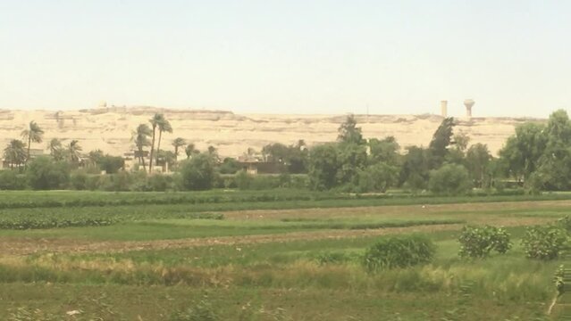 A view of the countryside along the river Nile from a passenger train that cuts through the heart of Egypt. An oasis of green contrasts against a horizon of dry sand and desert. 