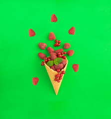 Ice cream cone with raspberries and red currants on the green  background. Top view. Copy space.