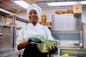 Happy black female cook working in restaurant and looking at camera.