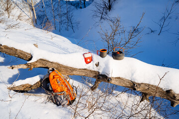 Trekking in the winter forest, a halt near a fallen tree, tourist equipment, a first aid kit with a backpack, metal utensils.