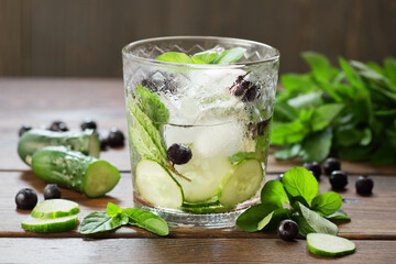 Cucumber and blueberry flavored with mint water or alcohol tonic cocktail on wooden table on dark...