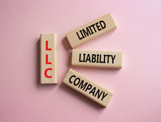 LLC - Limited liability company. Wooden cubes with word LLC. Beautiful pink background. Business and LLC concept. Copy space.