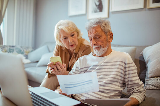 Senior couple reviewing documents and using smartphone and laptop at home