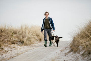 Mature man taking his border collie dog for a walk on the beach
