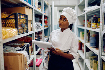 Black female chef examining stock of groceries while working in restaurant.