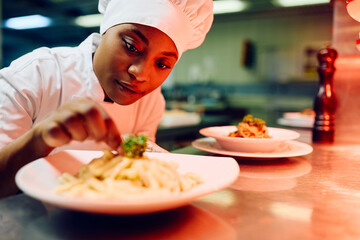 African American female chef decorating food plate cooking in kitchen.