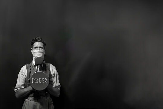 Libert&eacute; de la presse. Un journaliste homme a un b&acirc;illon sur la bouche qui l'emp&ecirc;che de parler dans le micro qu'il tient devant lui. Fond noir copyspace. 3 mai journ&eacute;e de la libert&eacute; de la presse.