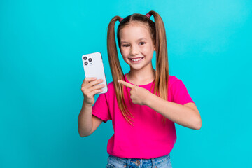 Photo of positive cheerful schoolgirl with ponytails wear pink t-shirt directing at smartphone in...