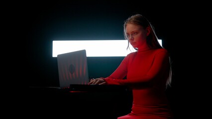 Young female with laptop against digital wall in dark club. Woman silhouette sitting typing on...