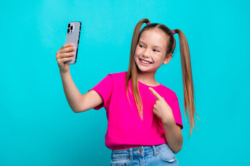 Photo of confident optimistic schoolgirl with ponytails directing at herself doing selfie on smartphone isolated on teal color background