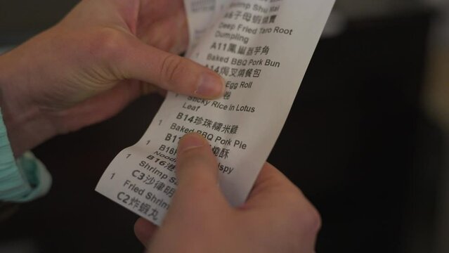 This video shows a close up view of anonymous hands reviewing a long dim sum receipt.
