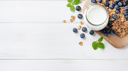 Fototapeta na wymiar Healthy breakfast ingredients. Homemade granola in open glass jar, milk or yogurt bottle, blueberries and mint on white wooden background, top view, copy space