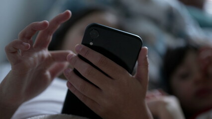 Close-up child hand using cellphone device, kid scrolling social media with fingers lying in bed
