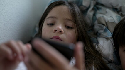 Little girl holding smartphone device looking at screen consuming media entertainment online. 8...