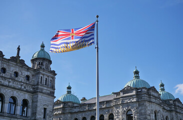 Flag of British Columbia waving in front of the Legislative Assembly of British Columbia Parliament...