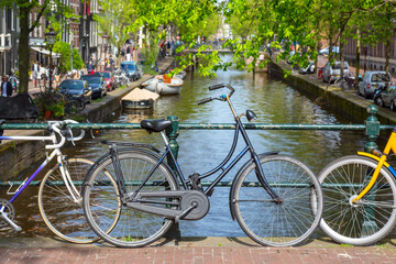 Fototapeta na wymiar Bicycles on the bridge in Amsterdam, Netherlands against a canal and old buildings during summer sunny day. Amsterdam postcard iconic view. Tourism concept.