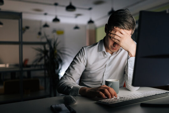 Tired businessman working in evening office alone. Exhausted anxious manager losing failure working on computer at late night. Stressed business man at workplace in office holding head on hands. - Powered by Adobe