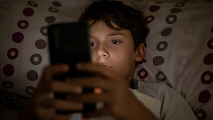 Child addicted to smartphone browsing social media lying in bed suffering from insomnia and...