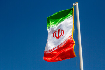 Waving Iran flag against blue sky.